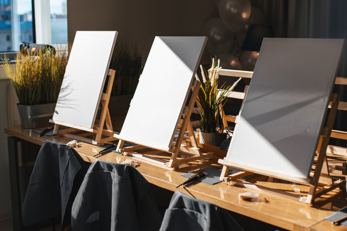Three blank canvases on easels with a blurred indoor background