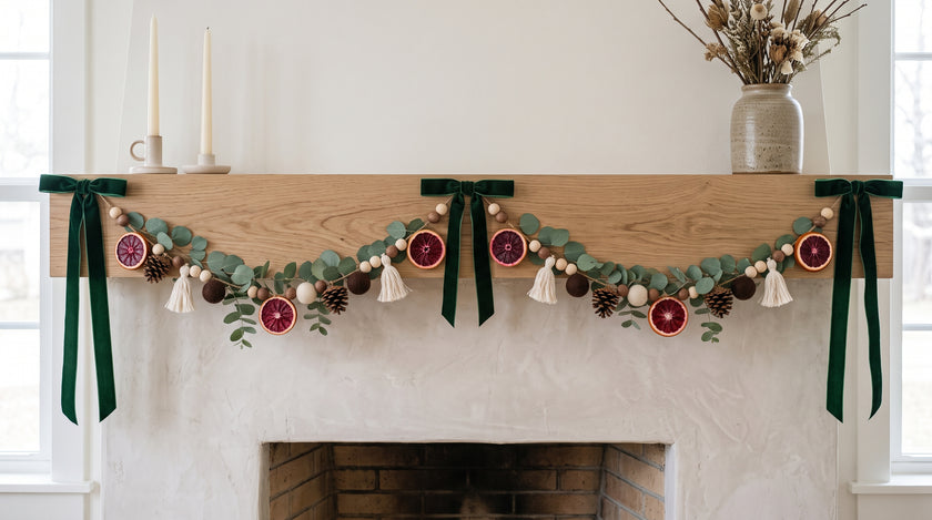 Blood orange and eucalyptus garland with pine cones, felt balls and green velvet bows on a mantel