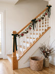 Eucalyptus, blood orange and pine cone garland with green velvet bows on a staircase railing