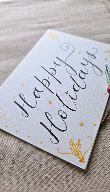 Hand-lettered Happy Holidays calligraphy card with gold stars and pine accents