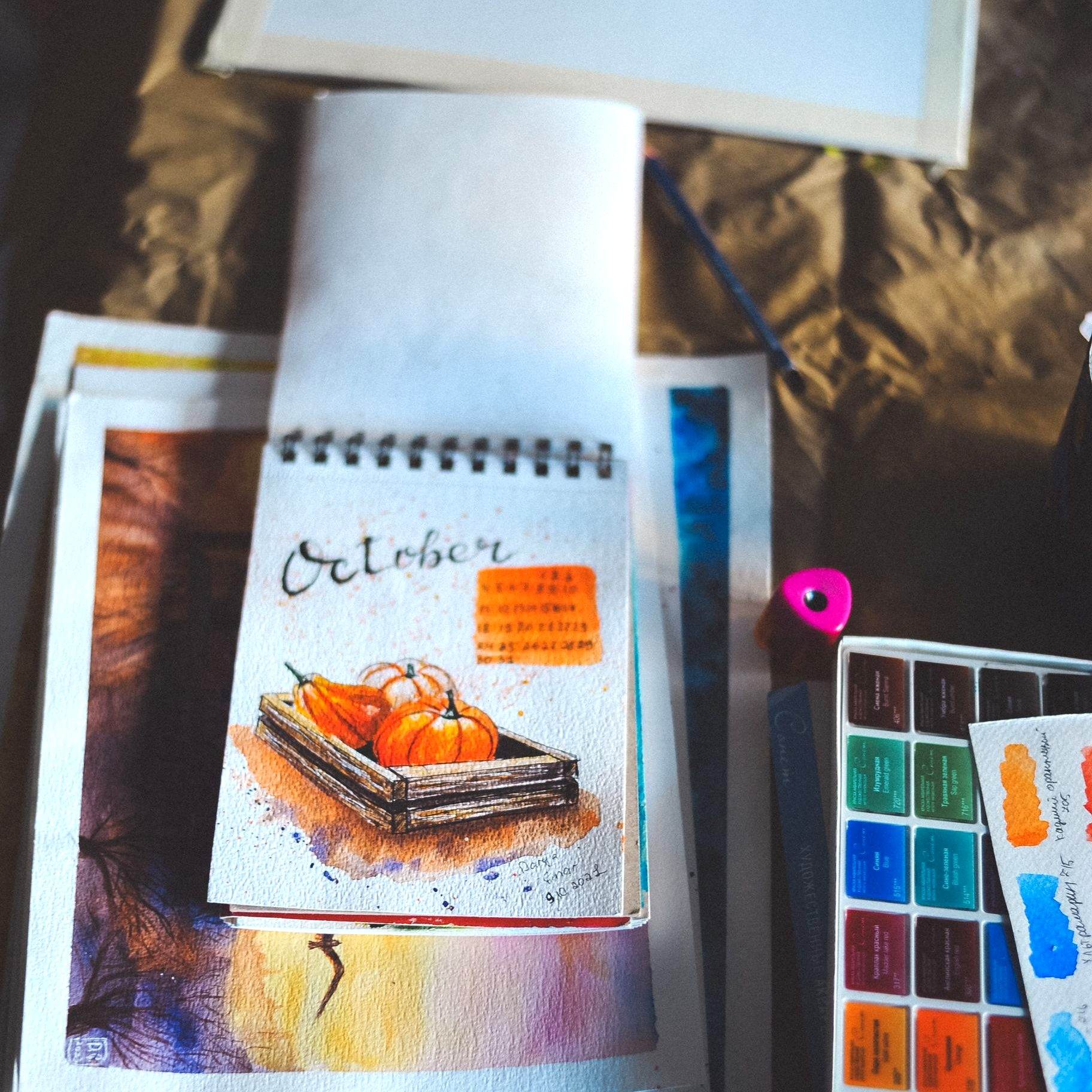 Loose watercolor sketchbook painting of autumn pumpkins beside a watercolor palette