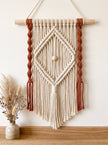 Cream and rust macramé wall hanging with a diamond pattern and wood bead on a wooden dowel