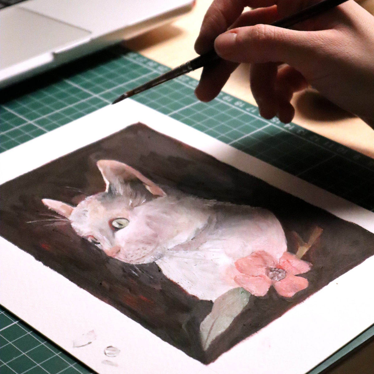 Gouache portrait of a white cat in progress with the artist's brush in hand