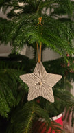 White textured plaster star ornament hanging on an evergreen tree